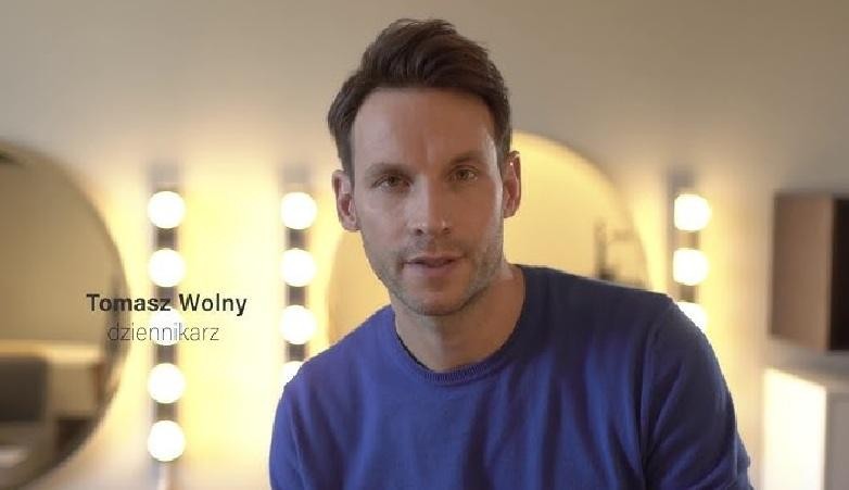 Tomasz Wolny, prezenter telewizyjny, w trakcie prowadzenia programu, w dynamicznej pozie, w nowoczesnym studiu.