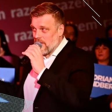 Adrian Zandberg przemawiający na wiecu politycznym, w tle tłum zwolenników, energiczna atmosfera.