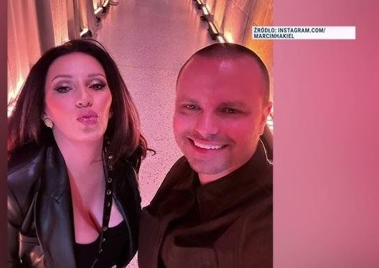 Marcin Hakiel uśmiechnięty, stojący w jasnym, nowoczesnym wnętrzu, ubrany w swobodny strój, symbolizujący jego życie prywatne i działalność pozataneczną.