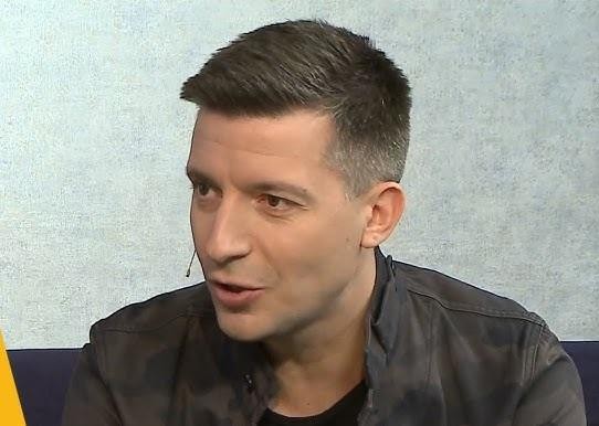 Michał Cessanis podczas pracy, być może prowadzący program telewizyjny lub prelekcję, otoczony elementami nawiązującymi do podróży i mediów.