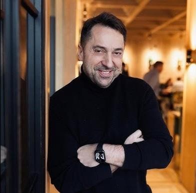 Marcin Miller, uśmiechnięty, oparty o luksusowy samochód, prezentujący swoje zamiłowanie do motoryzacji.