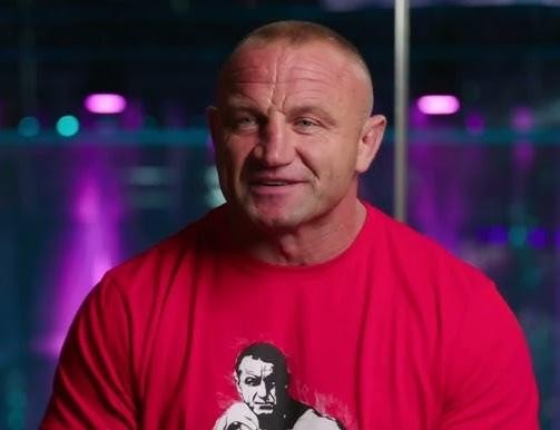 Mariusz Pudzianowski z bliska, z intensywnym wyrazem skupienia i determinacji na twarzy, pot widać na czole.
