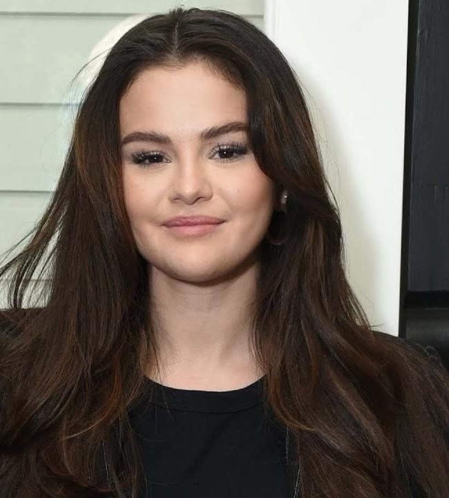 Selena Gomez na scenie podczas koncertu, śpiewająca z mikrofonem, z dynamicznym oświetleniem w tle.
